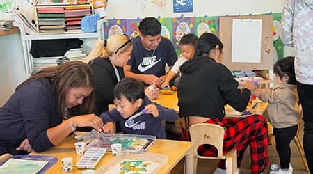 Parents and young children paint together around a classroom table during a playgroup