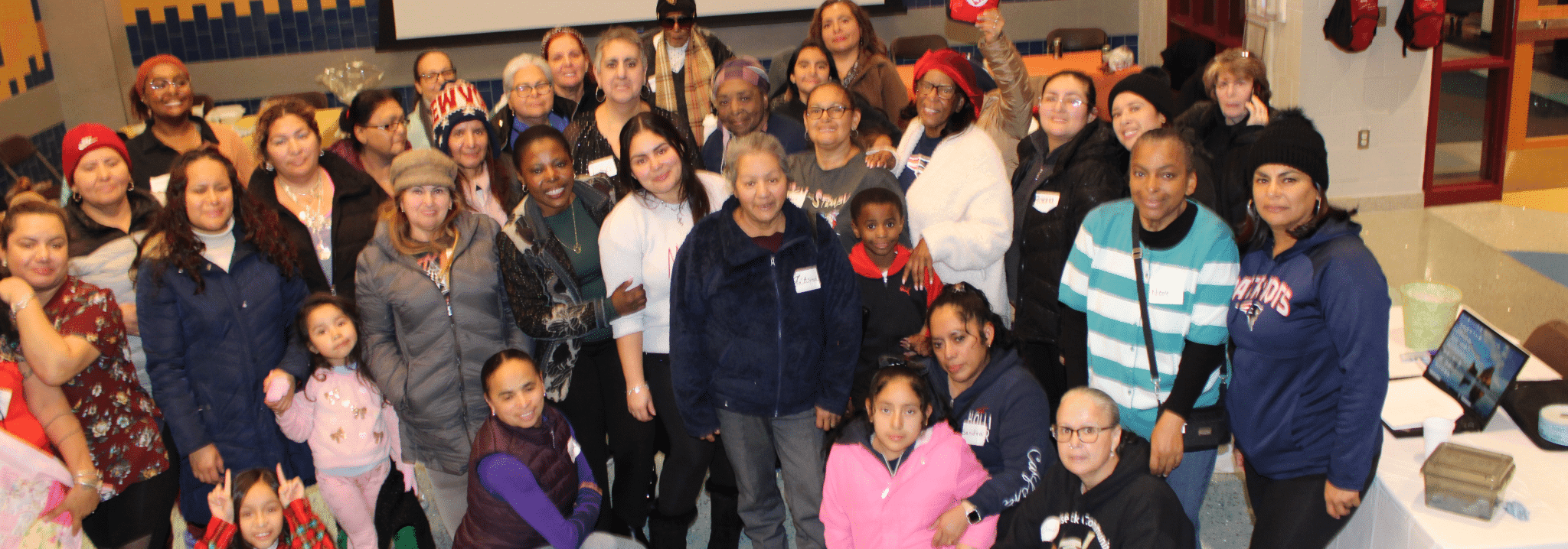 A large group of smiling parents, caregivers, and children gathered for a community event at FNC Chelsea