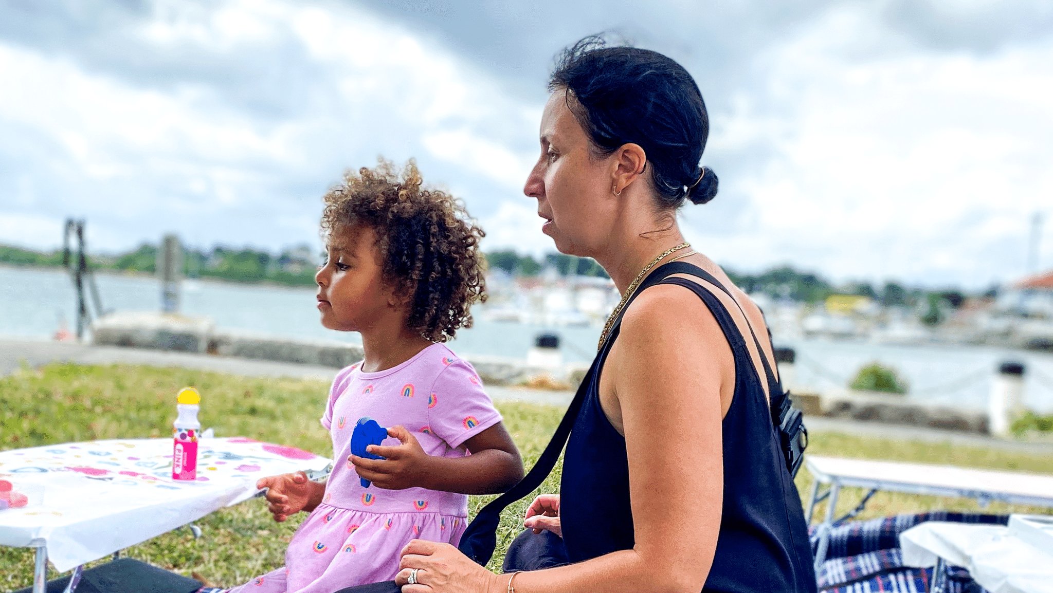 A caregiver and young child sit together at a waterfront playgroup table
