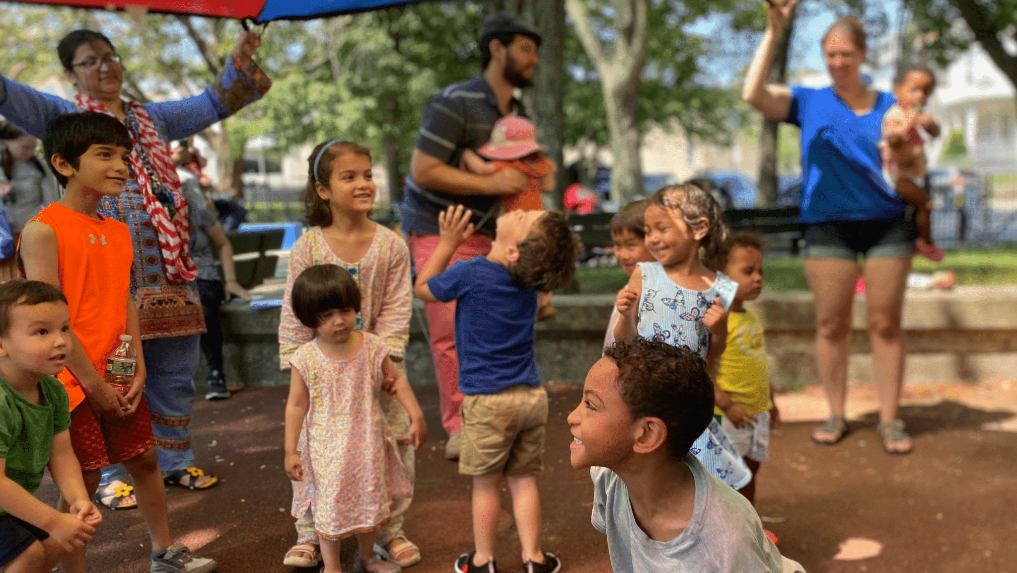 Children and caregivers play a parachute game together at an outdoor Family Nurturing Center playgroup
