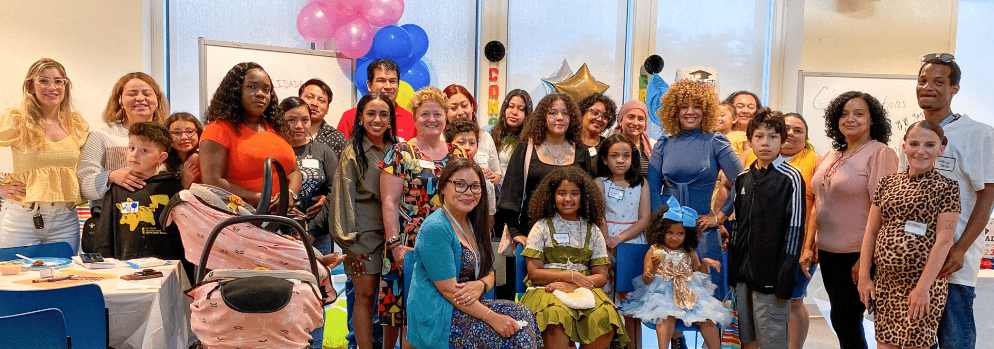 Families and staff gather for a group photo, with balloons behind them, at a Nurturing Parents graduation celebration.
