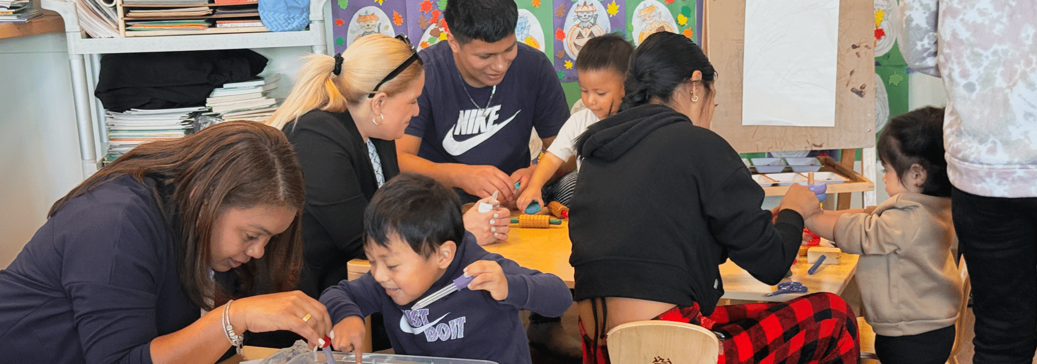Parents and young children play with modeling dough together around a table in a bright playgroup classroom.