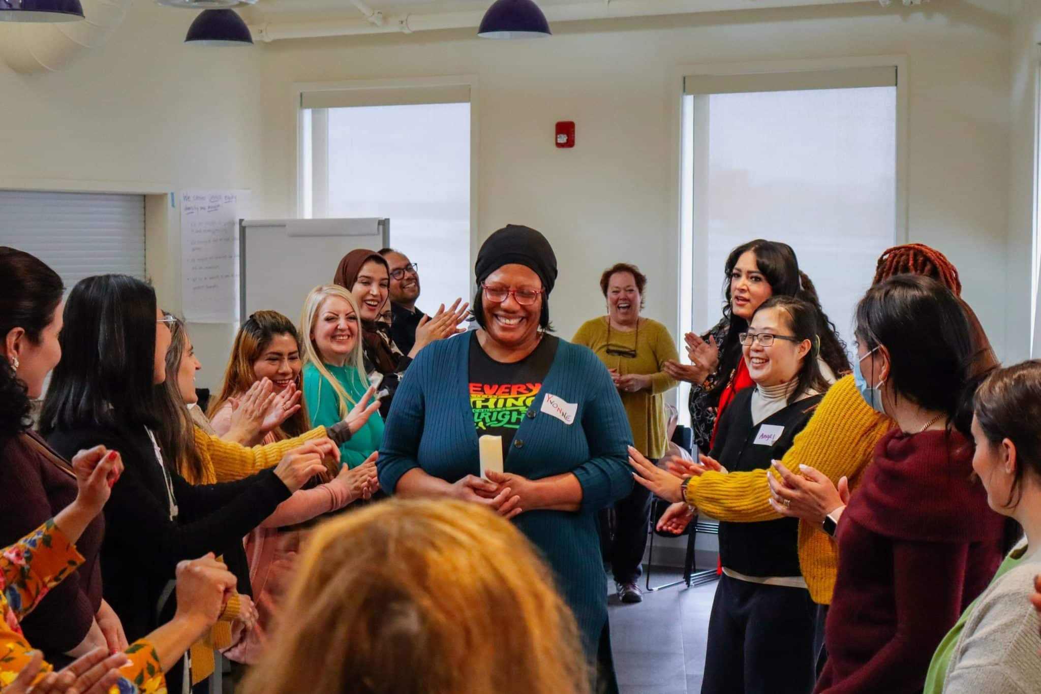 Providers and parent leaders applaud a smiling participant holding a candle at the center of a Family Nurturing Center training circle