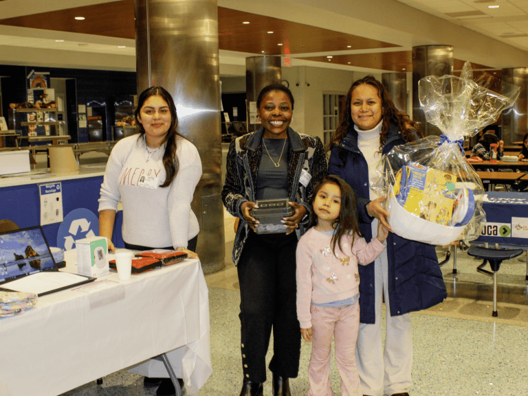 Staff and a family pose with a wrapped gift basket at a community resource fair