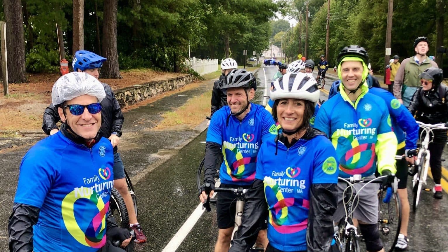 A group of Team FNC riders regroups on a wet, tree-lined road during the ride