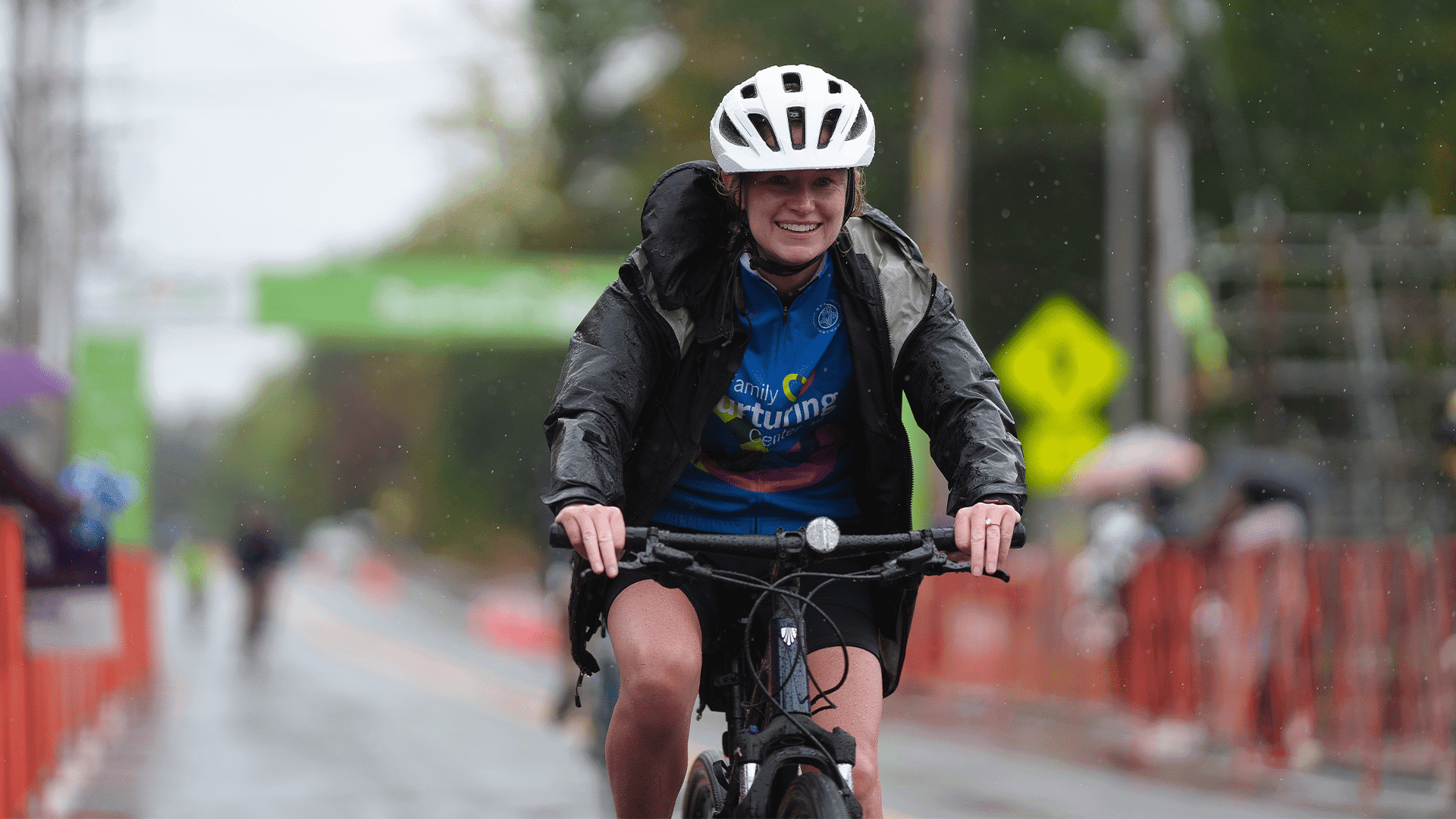 A rider in a white helmet smiles through the rain as she nears the finish line