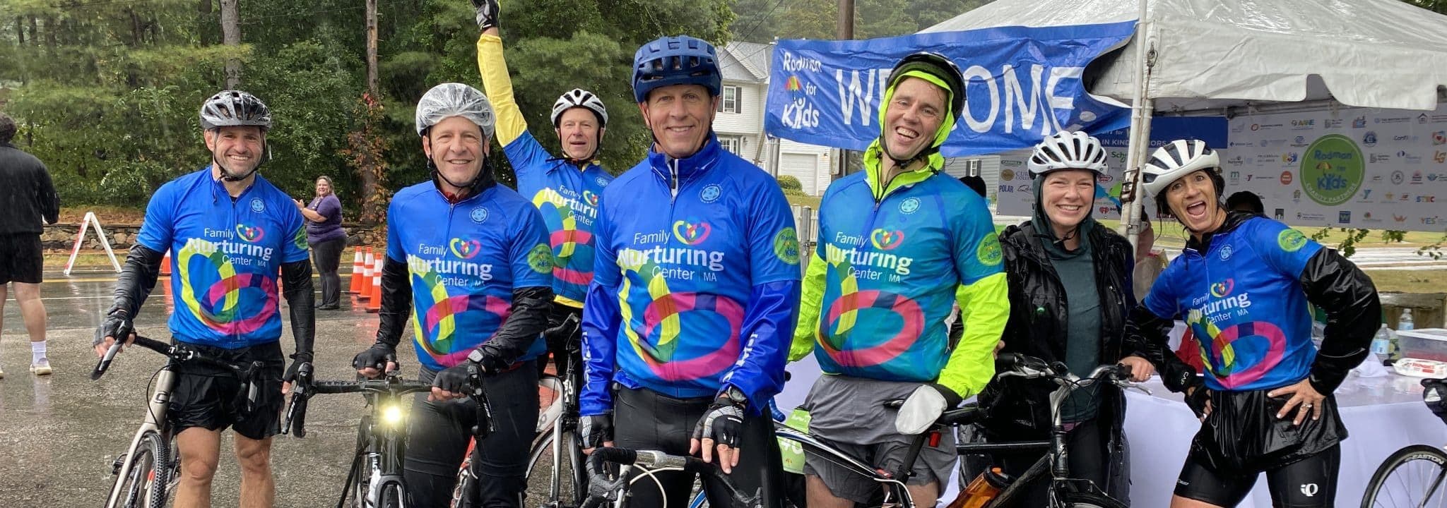 Team FNC cyclists in bright Family Nurturing Center jerseys smile at the Rodman Ride for Kids welcome tent.